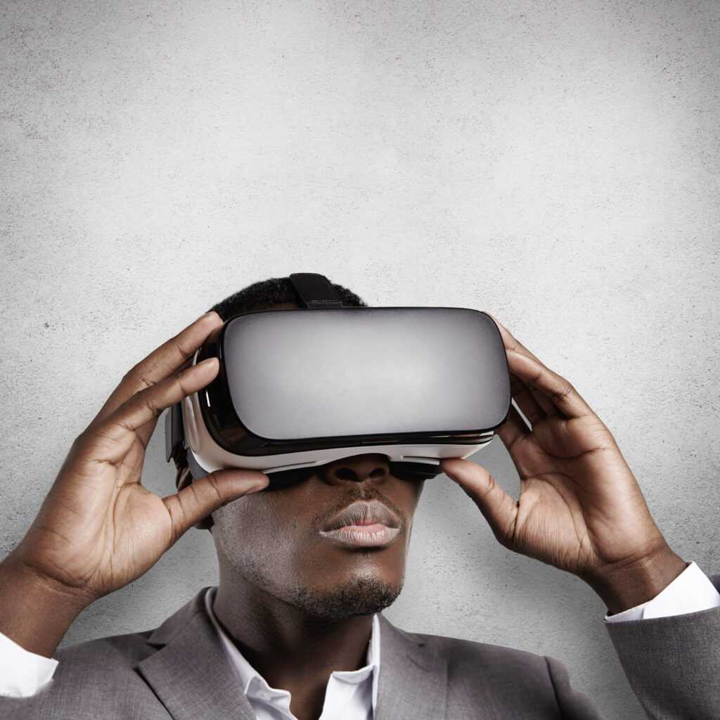 technology, science, innovation and cyberspace concept. portrait of young dark skinned employee wearing goggles in office. black man in formal wear experiencing virtual reality using 3d headset